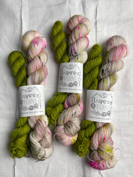 Three sets of hand dyed sock yarn comprising one 50g natural speckled and one 20g bright green on a white linen background.  The yarn is branded Inspiring Yarns.