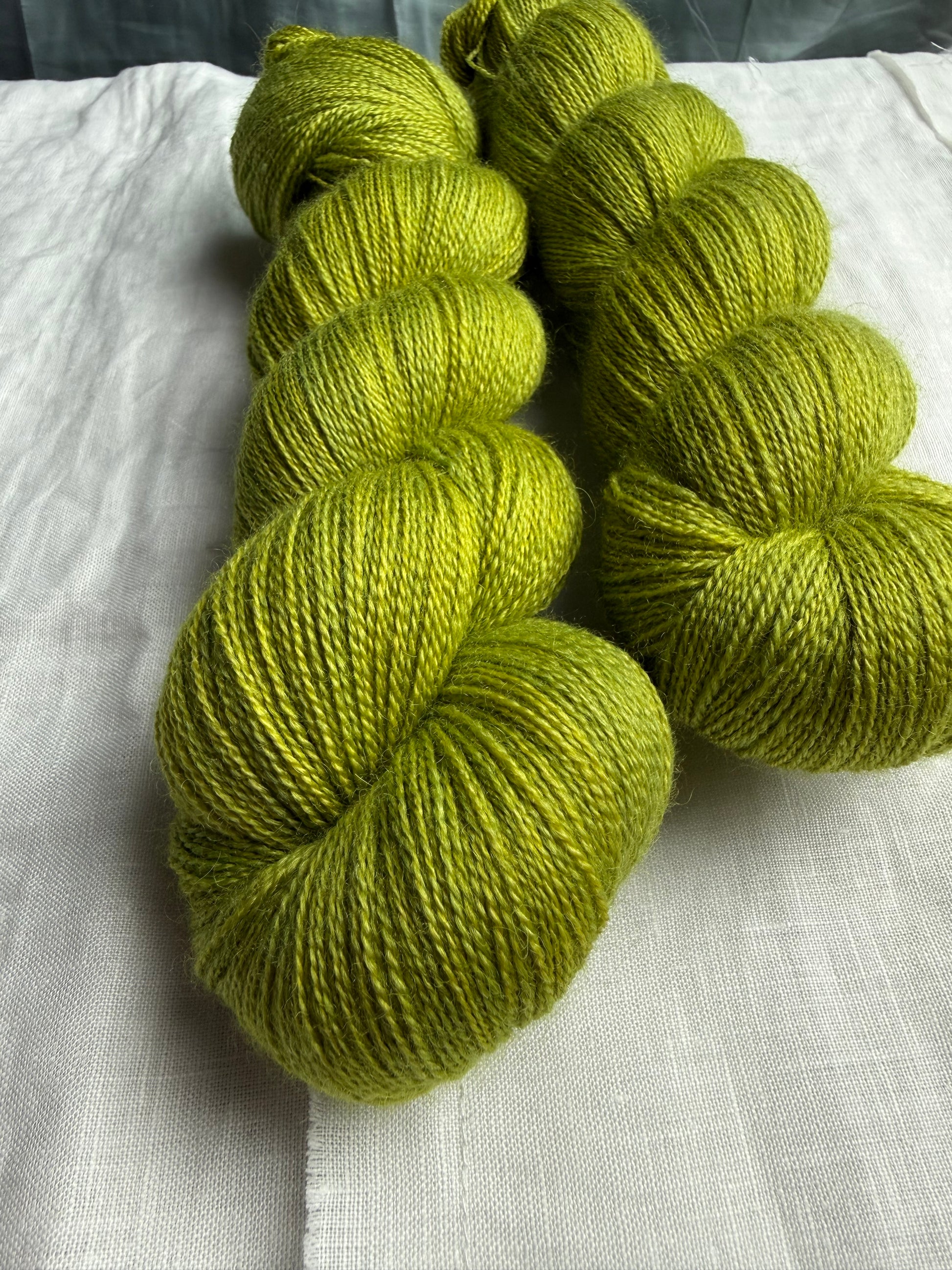 Two skeins of green yarn on a light white fabric background