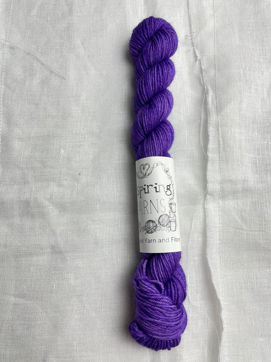 A bright purple coloured mini skein of Merino Smooth Sock yarn branded  Inspiring Yarns on a white linen fabric background. 