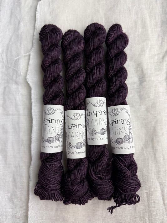 Four skeins of aubergine purple yarn with Inspiring Yarns labels on a light textured background.