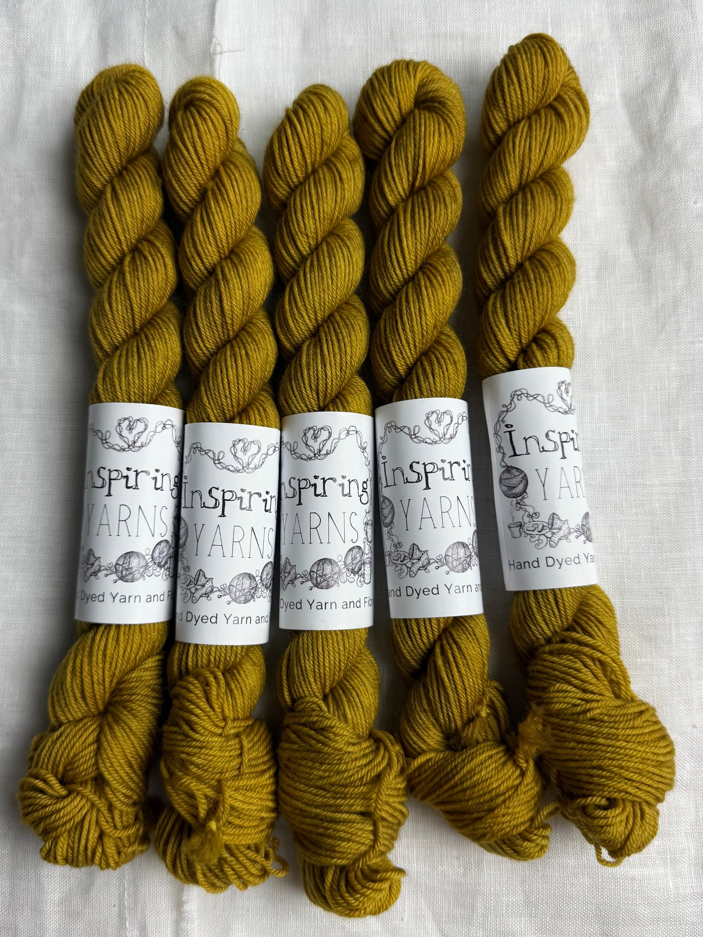 Five skeins of dark gold yarn with 'Inspiring Yarns' labels on a white background.