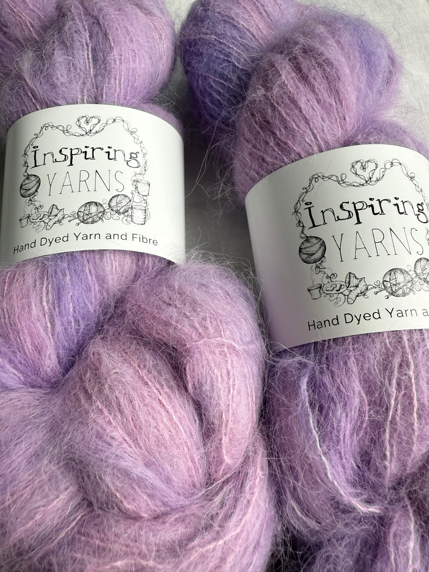 up close of two skeins of pink and lilac yarn with inspiring yarns labels and white background.