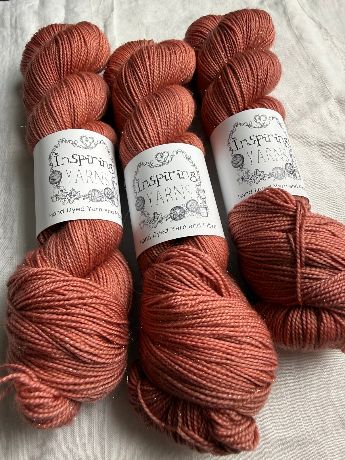 Close-up of three skeins of tonal warm terracotta yarn with Inspiring Yarns labels on a light textured background.