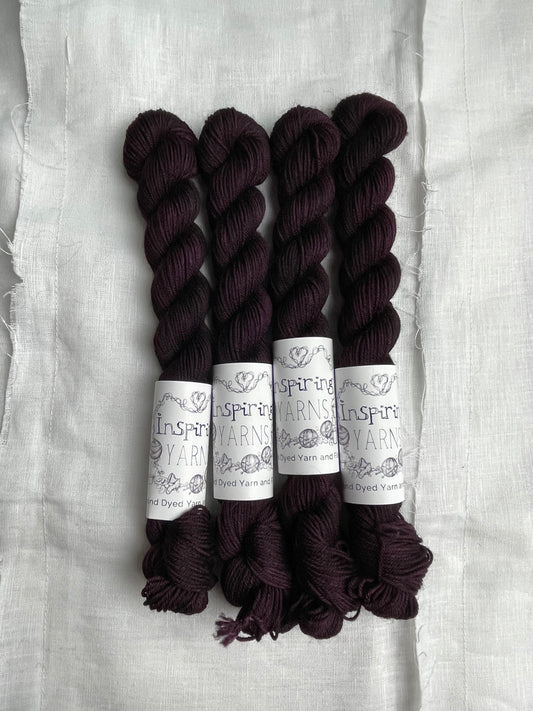 Four skeins of merino smooth sock yarn in a tonal dark burgundy colour labelled Inspiring Yarns on a white linen background. 