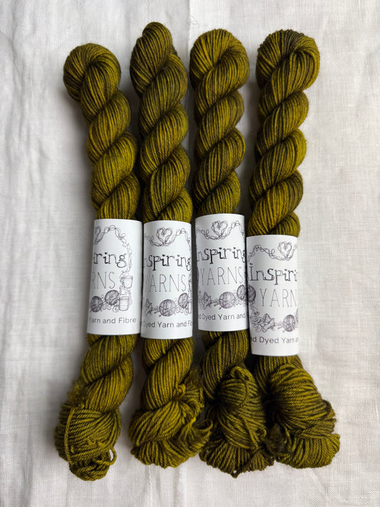 Four mini skeins of dark yellow green yarn labelled inspiring yarns on a white linen background