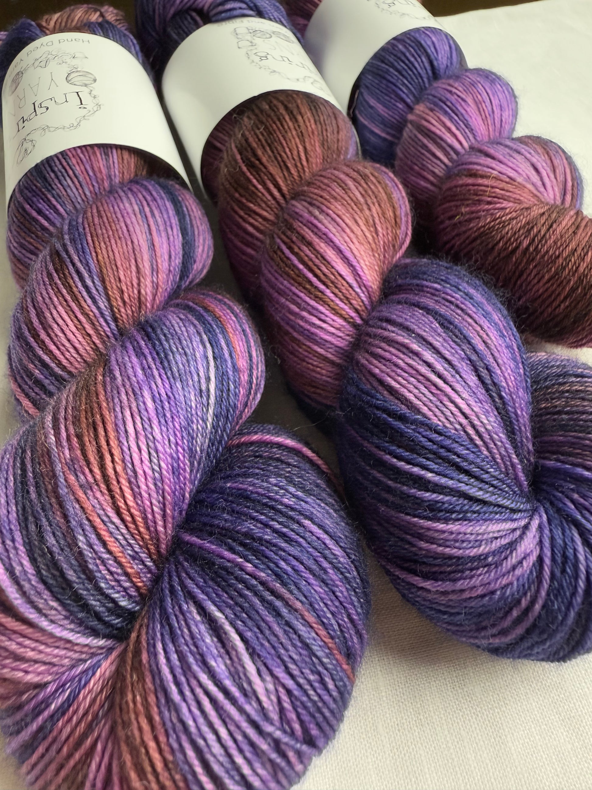 up close skeins of variegated yarn with purples, violets and browns. on white background and inspiring yarns label.