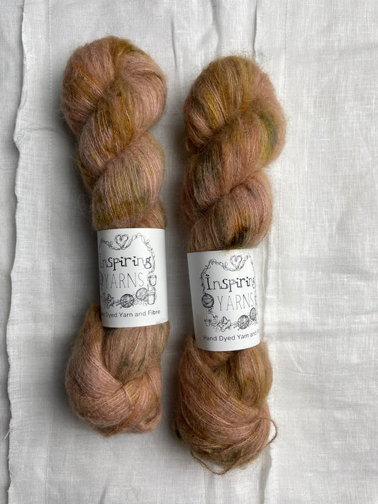 Two skeins of speckled soft terracotta hand dyed fluffy Alpaca Silk Lace yarn labelled Inspiring Yarns on a white linen background. 