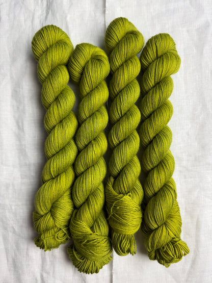 four skeins of bright green hand dyed yarn on a white linen background