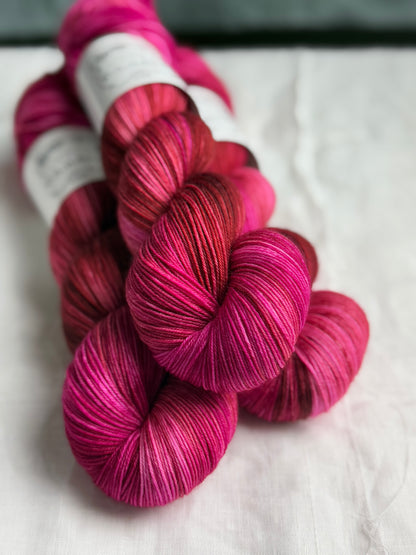 three skeins of pink and brown yarn stacked with labels out of view and a white background