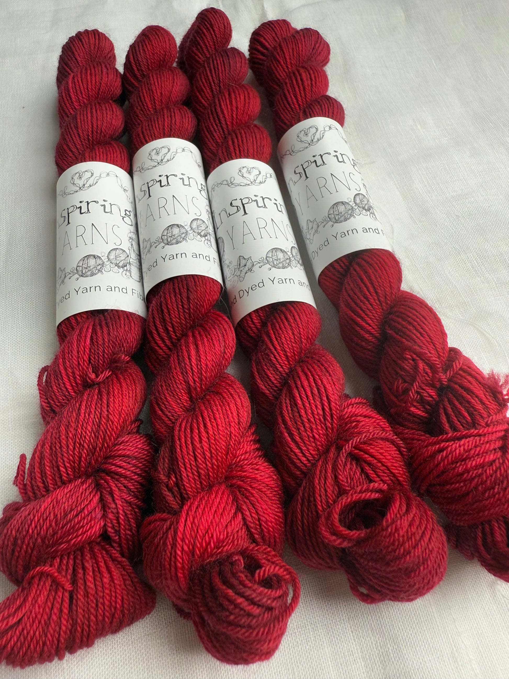 up close of skein of dark ruby red with inspiring yarns lbels on a white background.