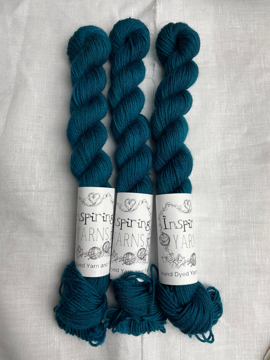 Three intense teal blue coloured mini skeins of Merino Smooth Sock yarn branded  Inspiring Yarns on a white linen fabric background. 
