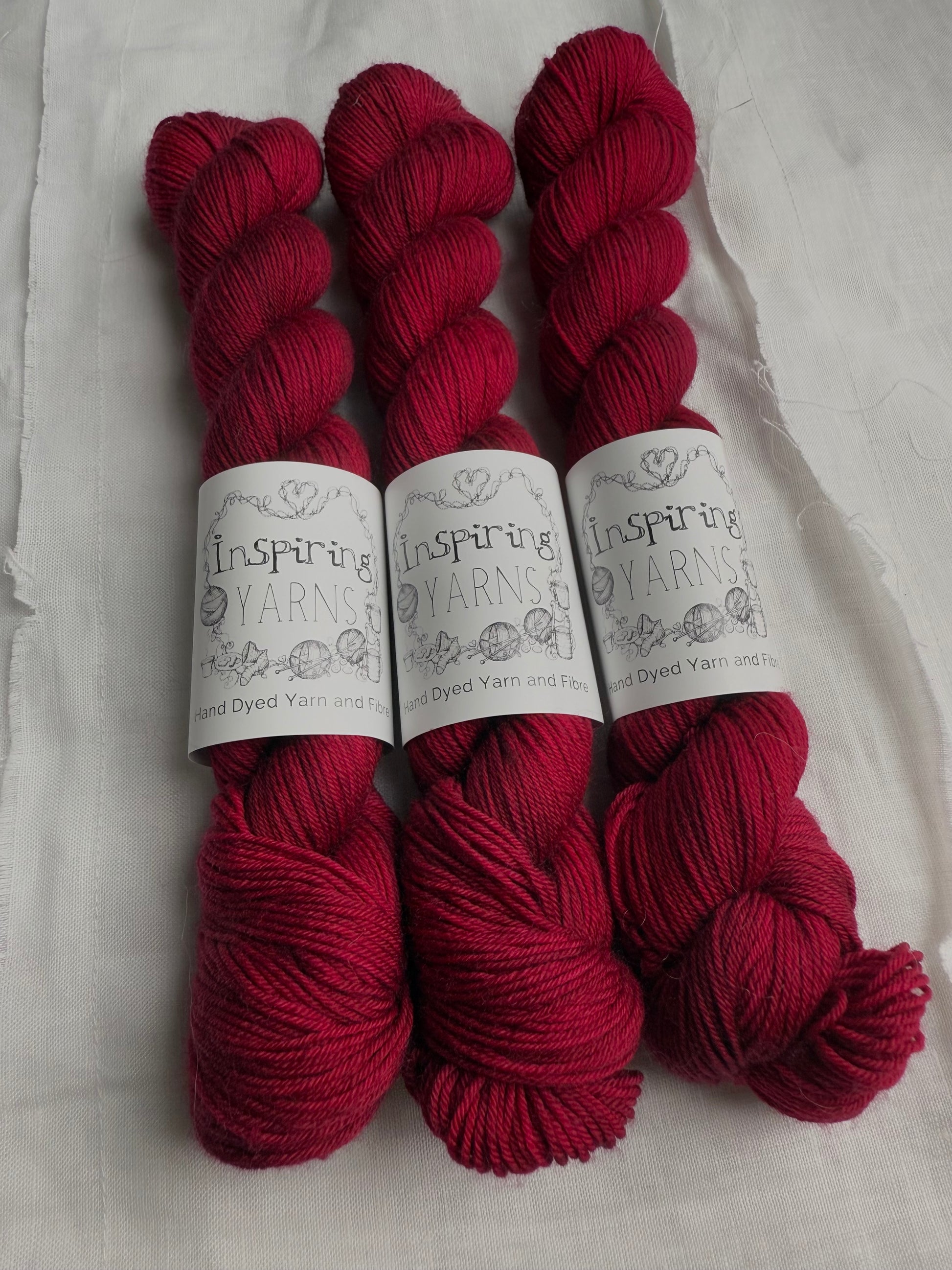 three skeins of dark ruby red yarn on a white background and inspiring yarns label around them.