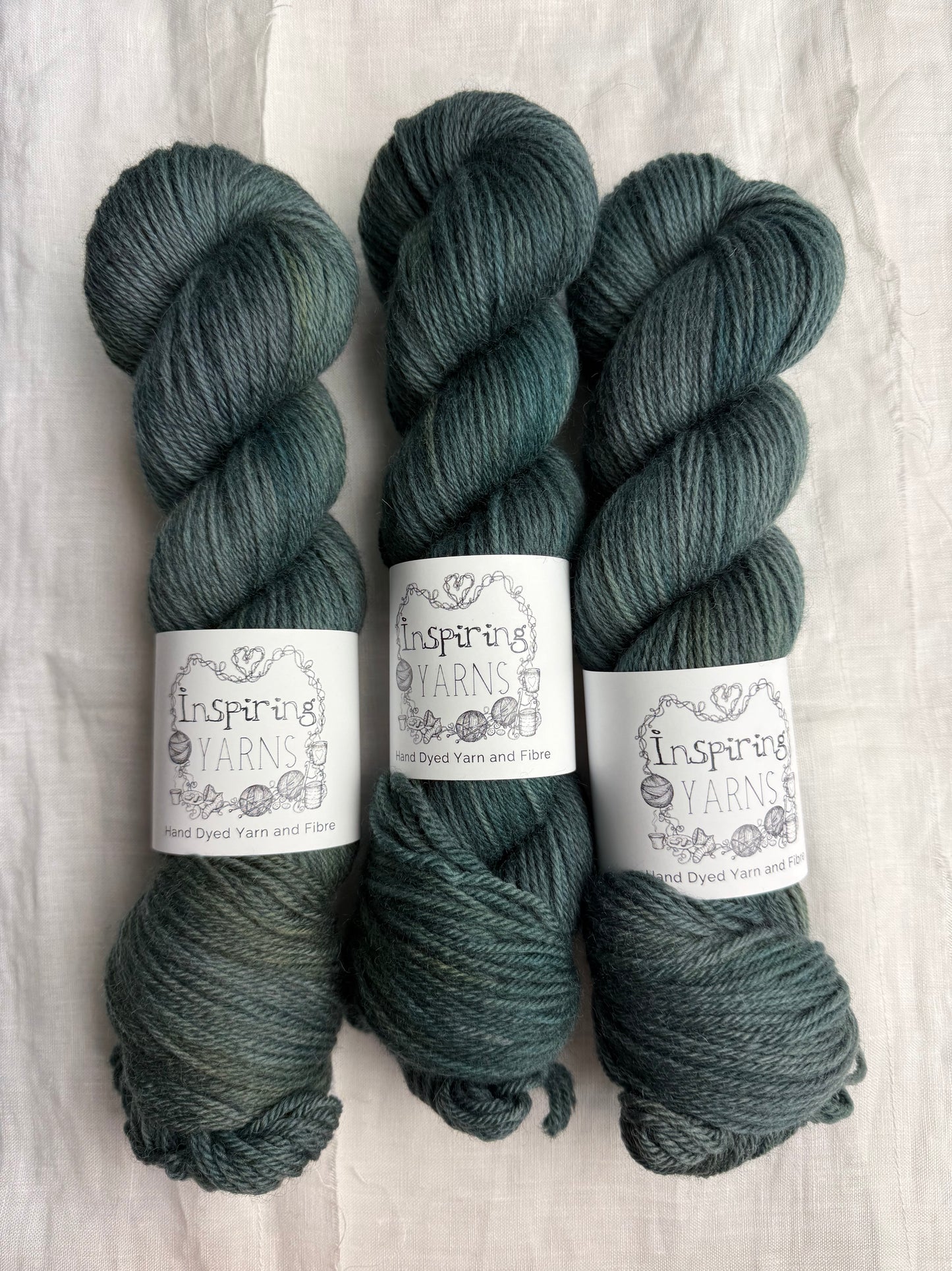 Three skeins of dark green tonal yarn labelled Inspiring Yarns on a white background