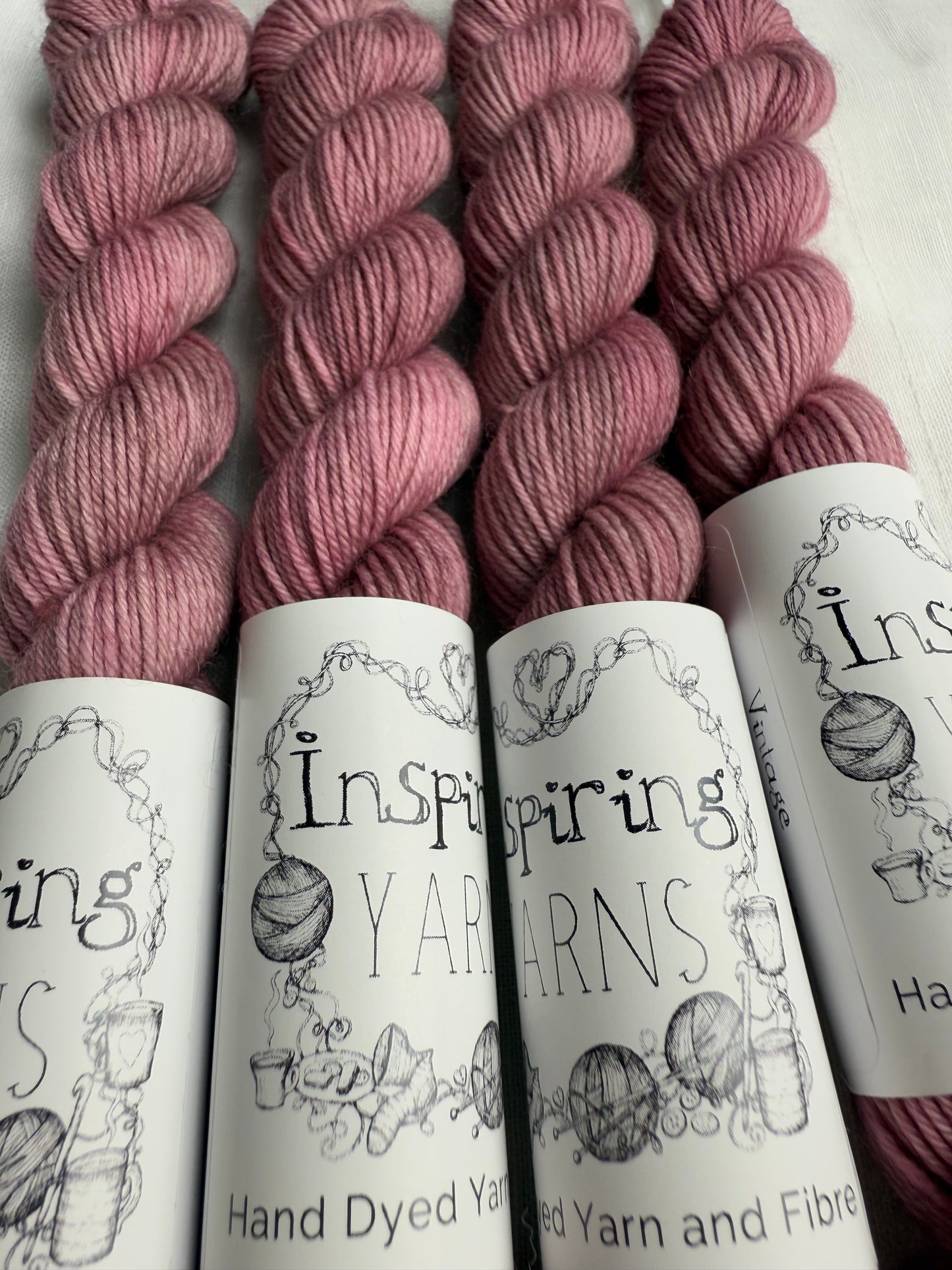 close up of 4 light dusky pink mini skeins with inspiring yarns label on white background. 