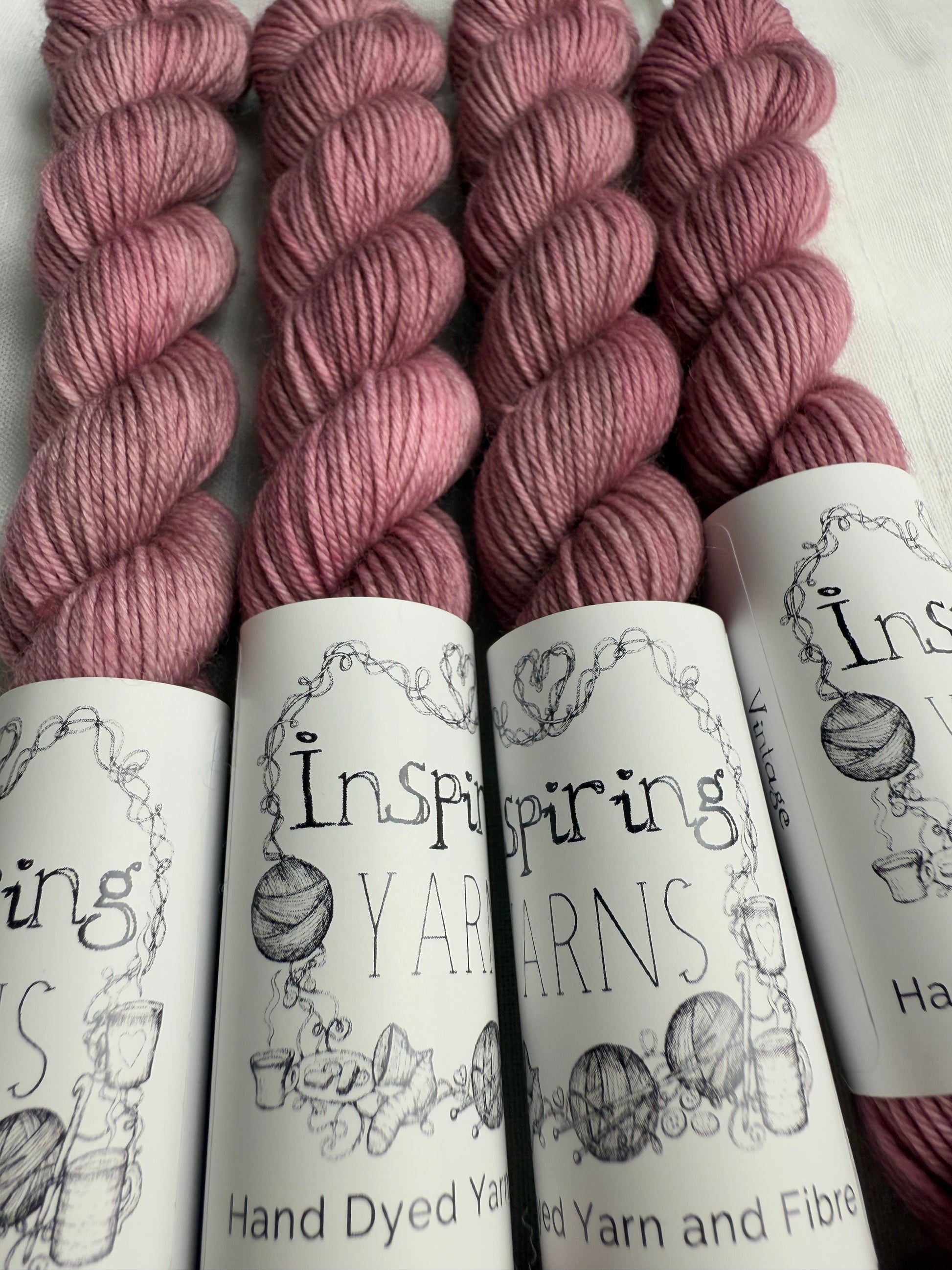 close up of 4 light dusky pink mini skeins with inspiring yarns label on white background. 