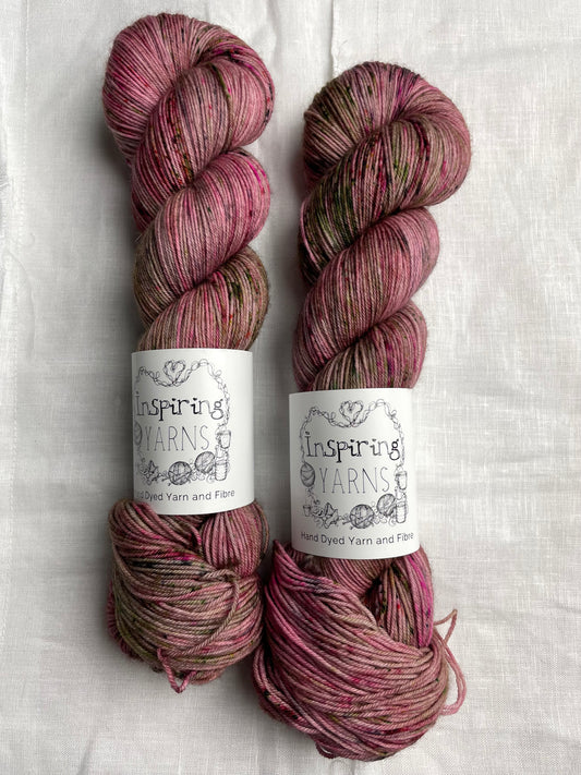 Two speckled pink coloured skeins of Merino Smooth Sock yarn branded  Inspiring Yarns on a white linen fabric background. 