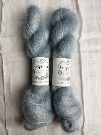 Two skeins of gray yarn with 'Inspiring Yarns' labels on a textured fabric background.