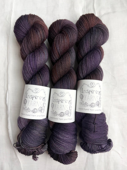three skeins of dark purple yarn with orange and blue tones with inspiring yarns label and white background.