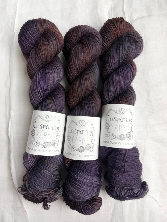 three skeins of dark purple yarn with orange and blue tones with inspiring yarns label and white background.