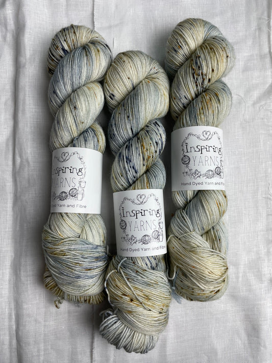 Three skeins of blue and brown speckled Merino Smooth Sock yarn labelled Inspiring Yarns on a white linen background.