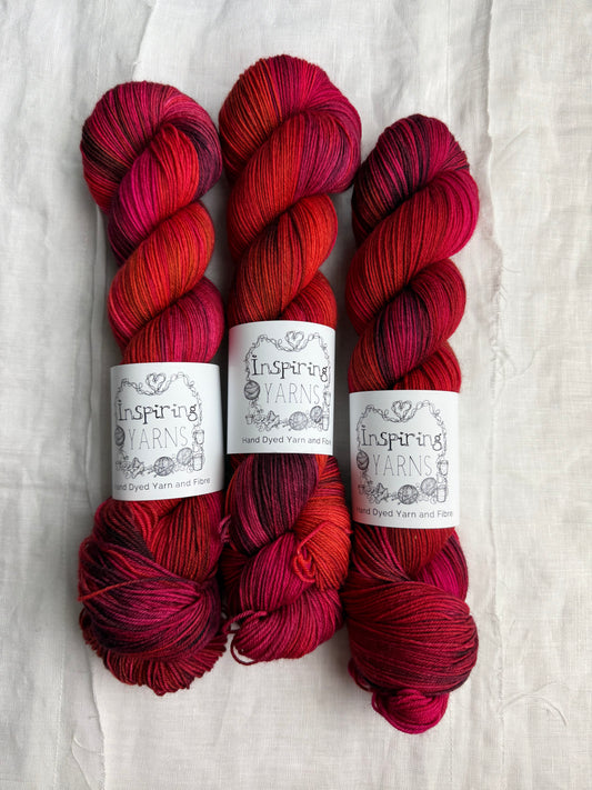 Three skeins of red variegated yarn labelled Inspiring Yarns on a white background