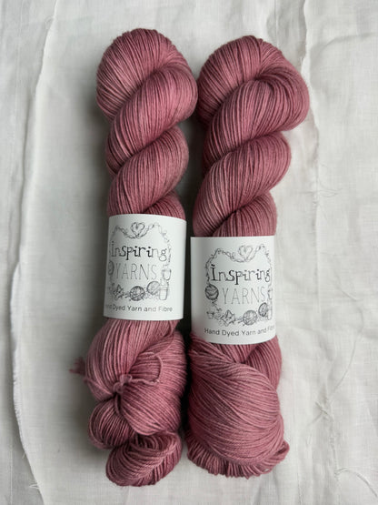 two skeins of light dusty pink yarn , with inspiring yarns label on white background.