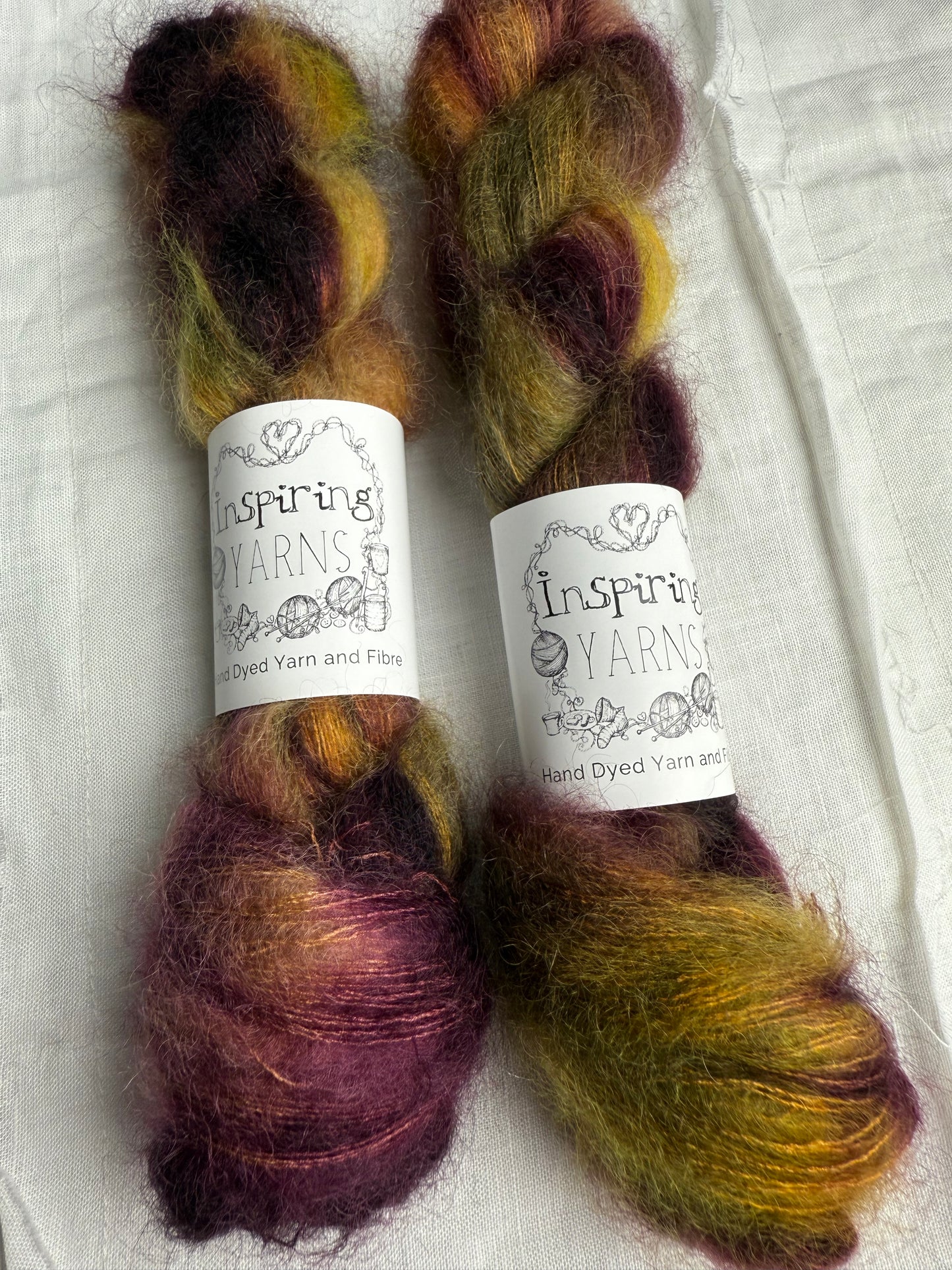 Two skeins of multicolored yarn with 'Inspiring Yarns' labels on a white fabric background.