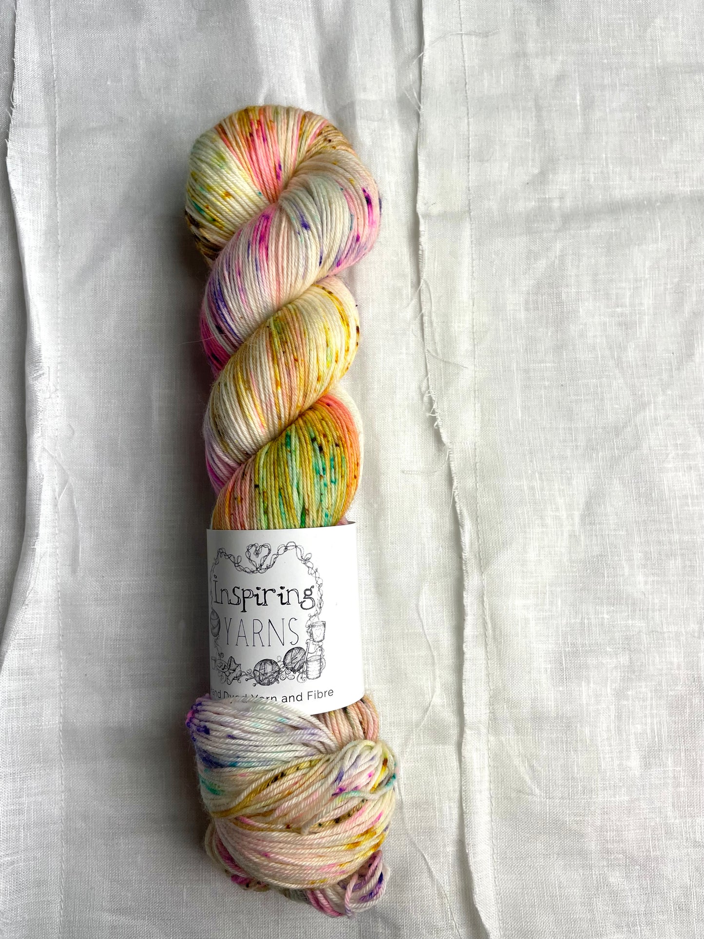 skein of natural coloured yarn and multicoloured speckles with inspiring yarns label and white background.