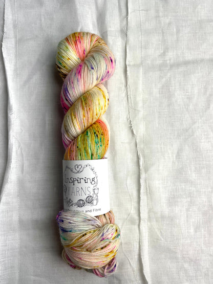 skein of natural coloured yarn and multicoloured speckles with inspiring yarns label and white background.