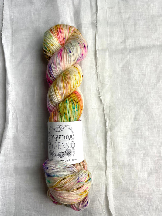 skein of natural coloured yarn and multicoloured speckles with inspiring yarns label and white background.