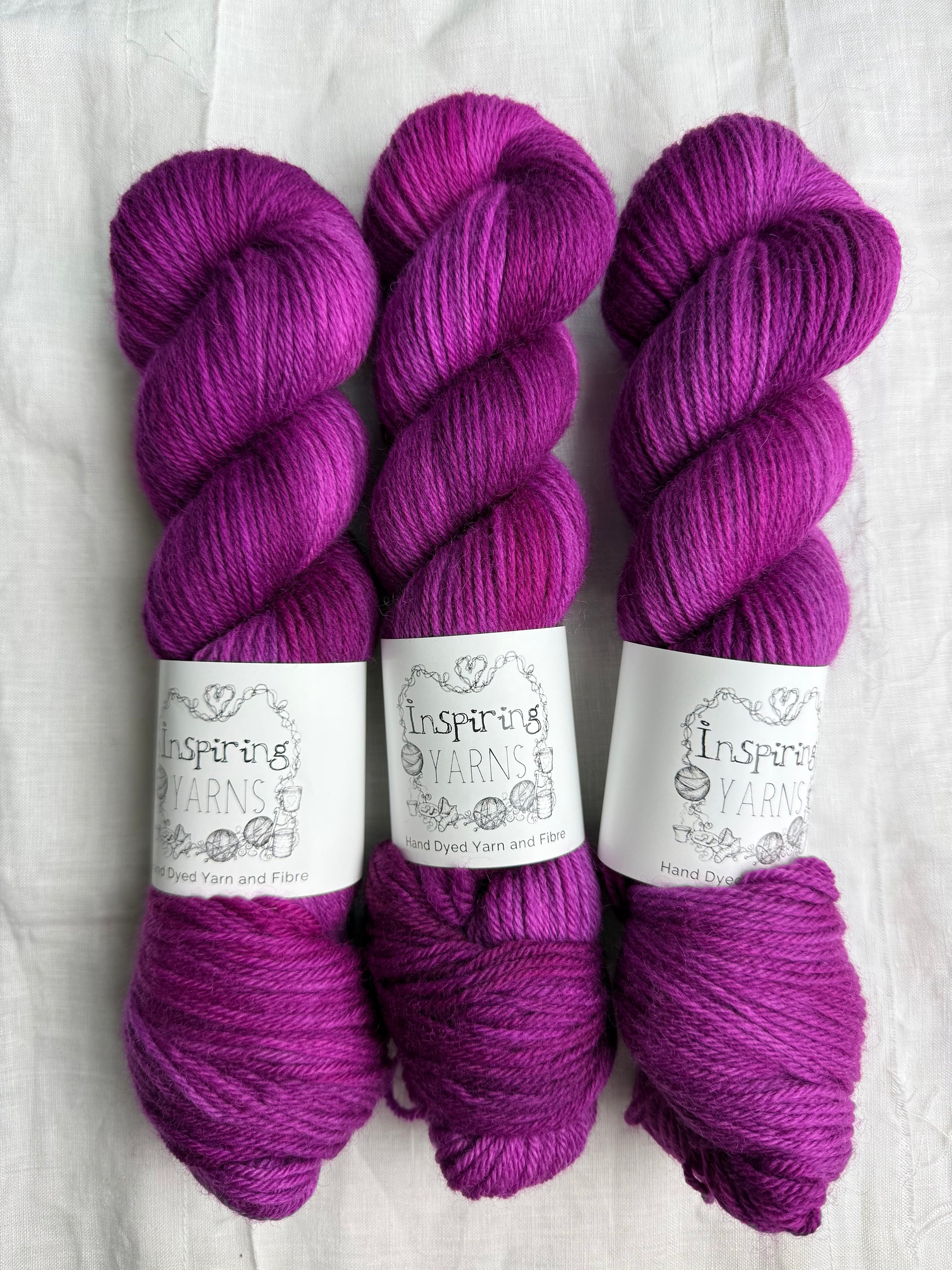 Three skeins of fuchsia tonal yarn labelled Inspiring Yarns on a white background