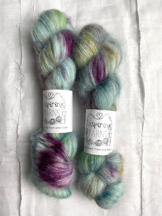 Two skeins of brushed suri silk in a light teal colour with coloured speckles labelled Inspiring Yarns on a white linen background. 