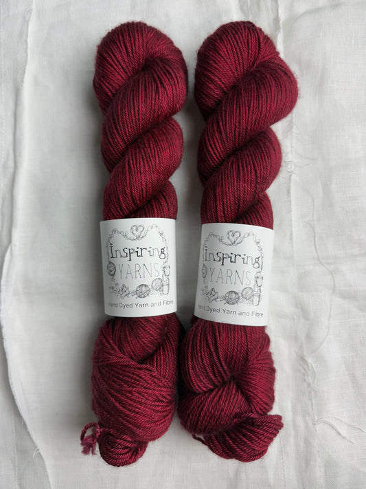 two skeins of yarn in a dark ruby red on a white background and inspiring yarns labels around them.