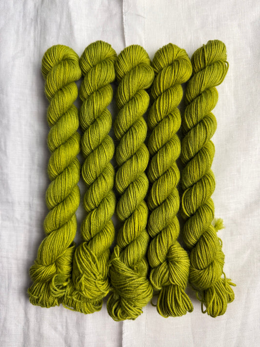Five skeins of green yarn on a white fabric background