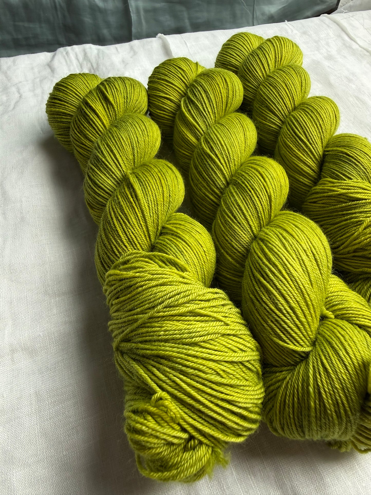 Three skeins of green yarn on a white fabric background
