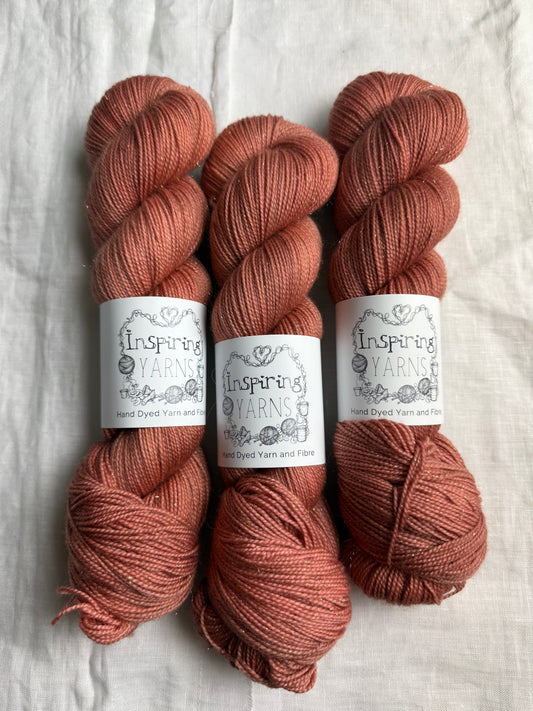 Three skeins of tonal warm terracotta yarn with Inspiring Yarns labels on a light textured background.