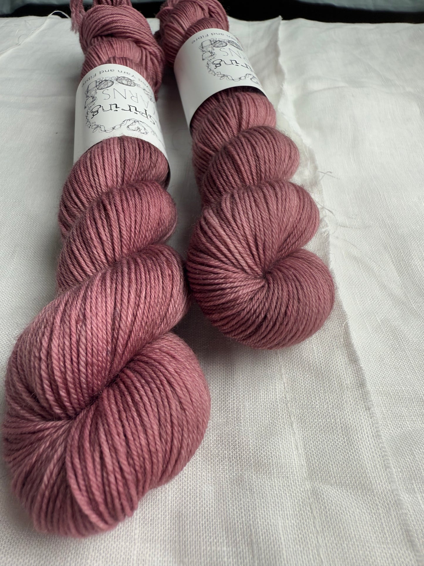 two skeins of dusty pink yarn, close up and at an angle with inspiring yarns label on a white background. 