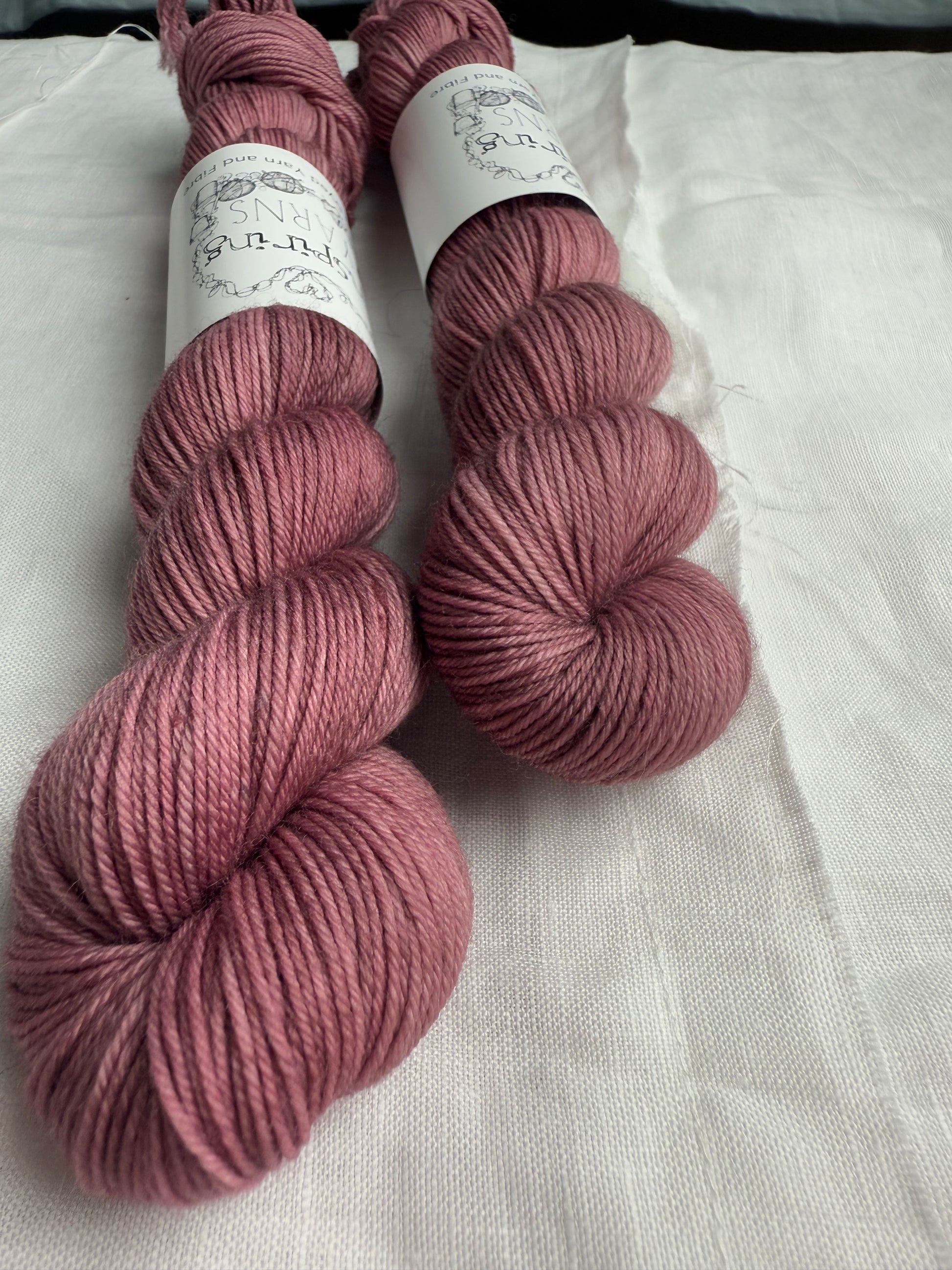 two skeins of dusty pink yarn, close up and at an angle with inspiring yarns label on a white background. 