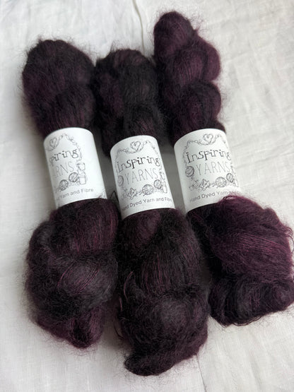 Three skeins of dark burgundy mohair yarn labelled Inspiring Yarns on a white linen fabric background