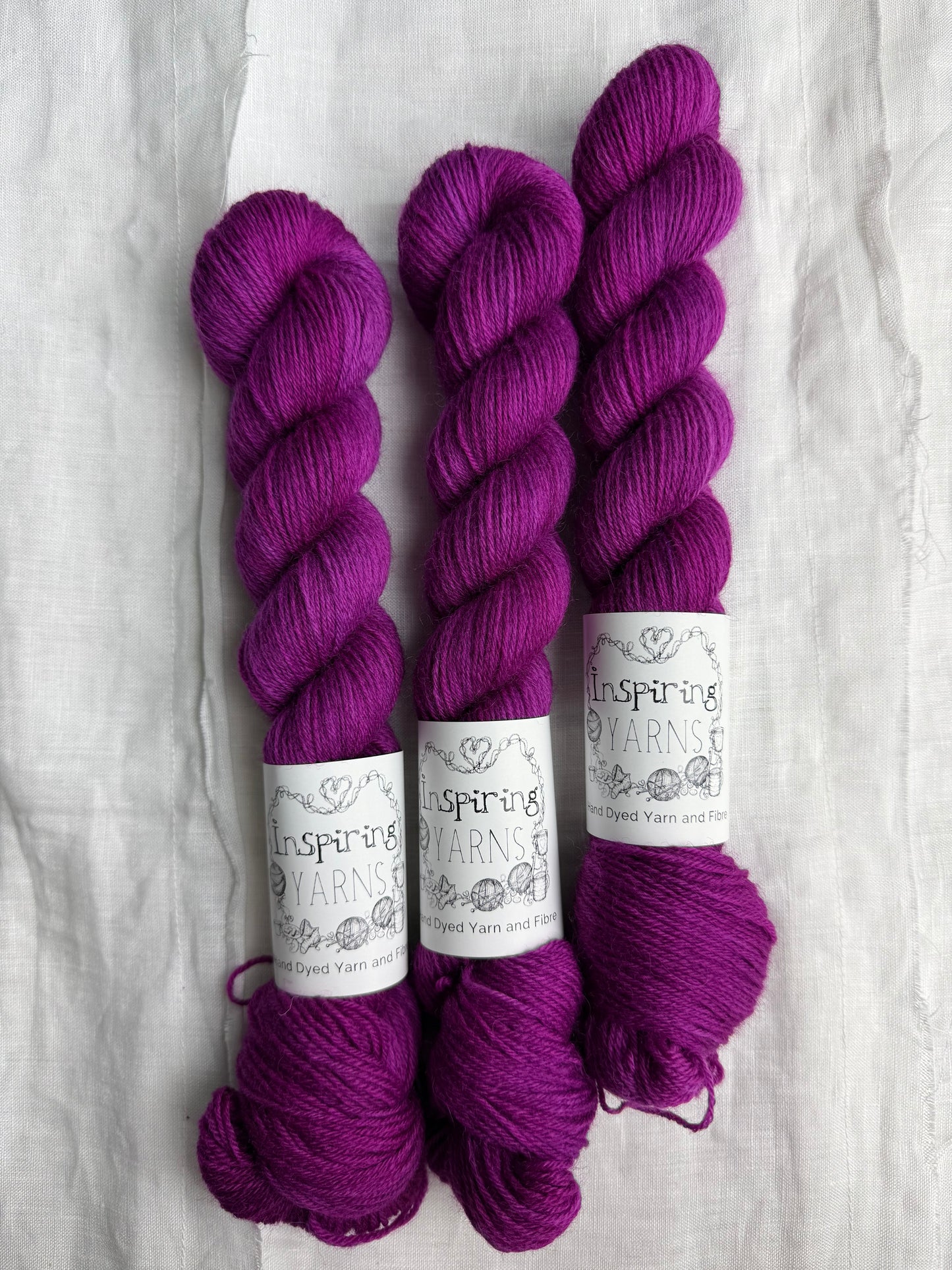 Three skeins of fuchsia tonal yarn labelled Inspiring Yarns on a white background