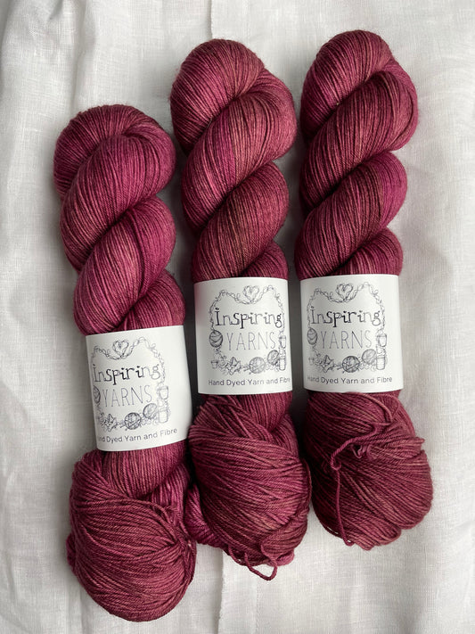 Three skeins of dusky pink Merino Smooth Sock yarn labelled Inspiring Yarns on a white linen background.