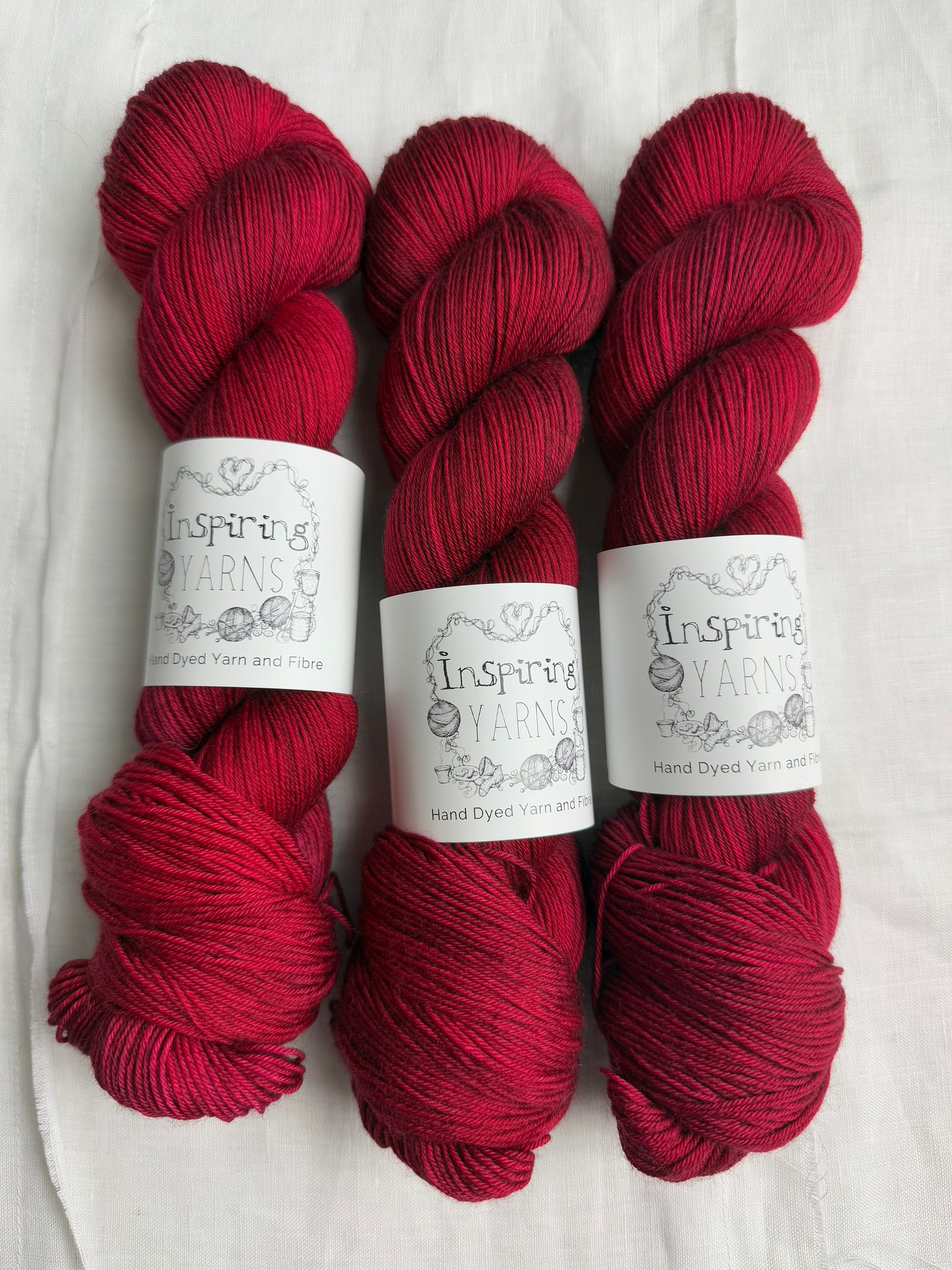 three skeins of dark ruby red yarn on a white background and inspiring yarns labels