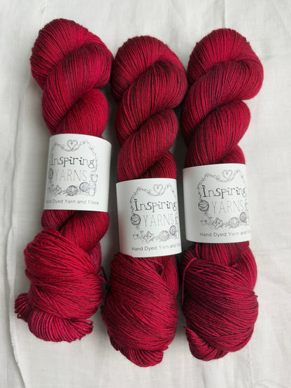 three skeins of dark ruby red yarn on a white background and inspiring yarns labels