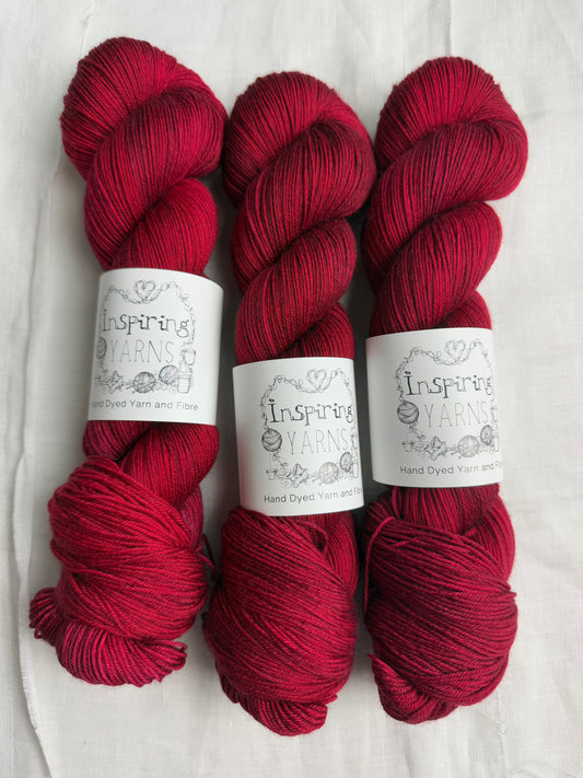 three skeins of dark ruby red yarn on a white background and inspiring yarns labels