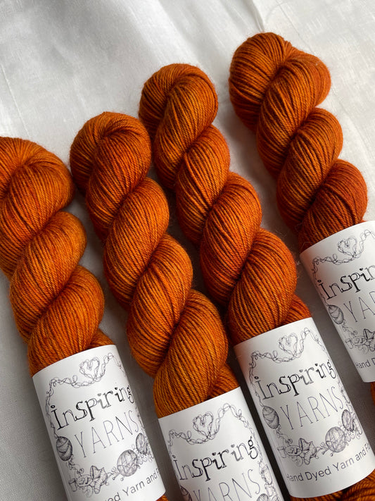 Close up image of four tonal burnt orange coloured skeins of hand dyed Merino Smooth Sock yarn branded Inspiring Yarns on white linen fabric.