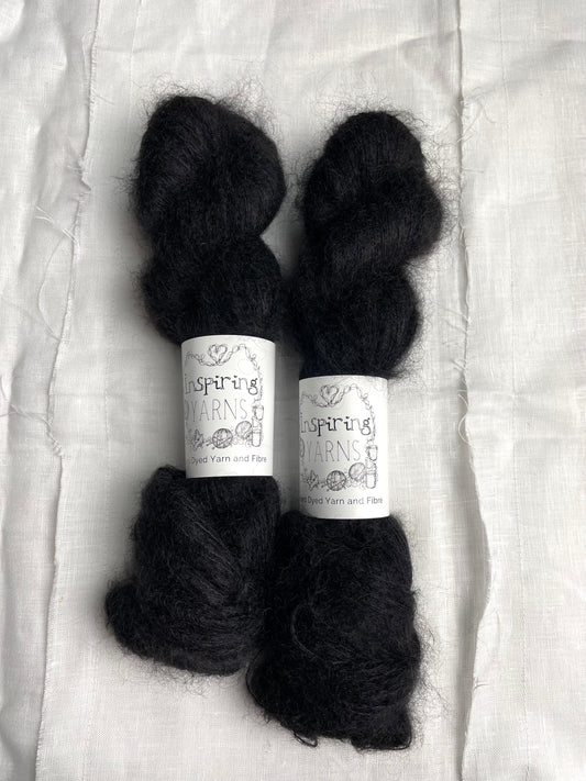 Two skeins of black coloured Kid Mohair Silk Lace labelled Inspiring Yarns on a white linen background.