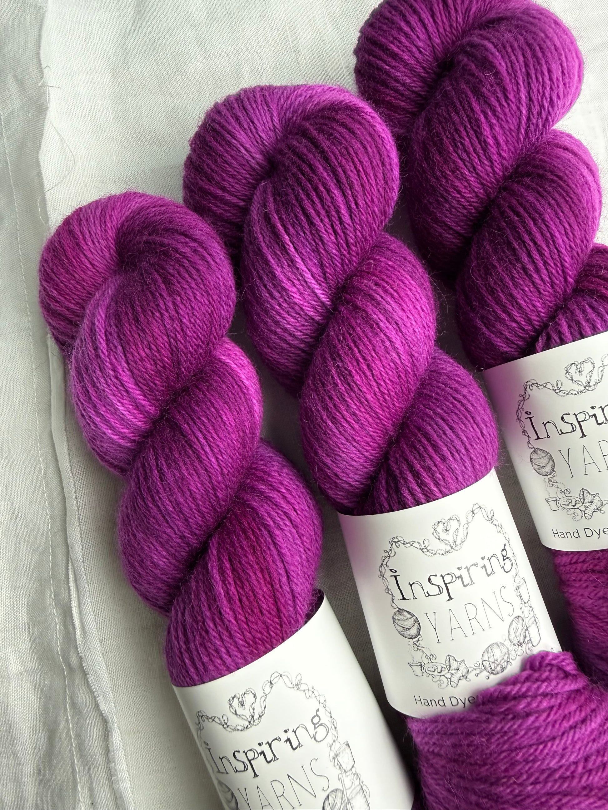 Three skeins of fuchsia tonal yarn labelled Inspiring Yarns on a white background