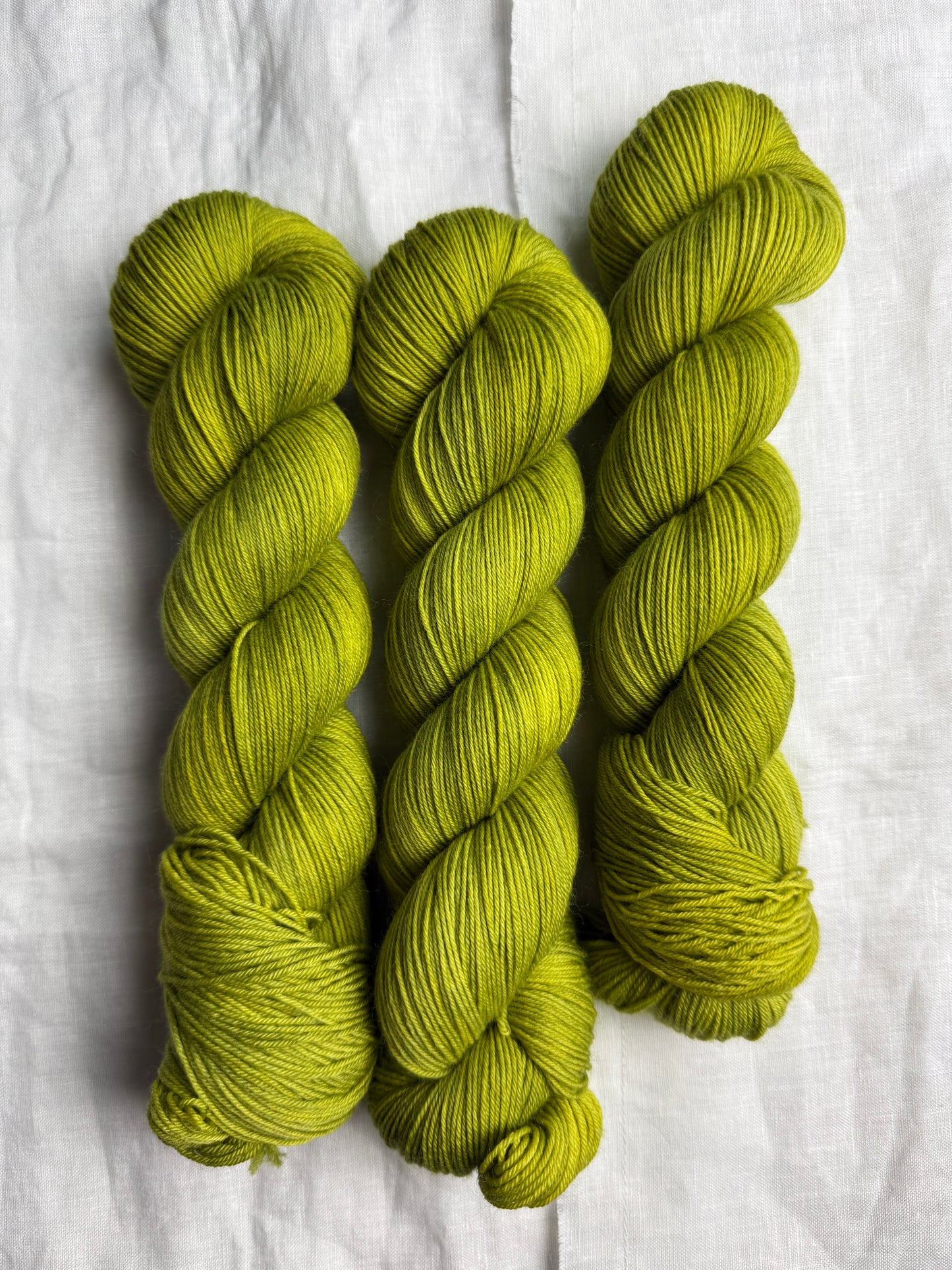 Three skeins of green yarn on a white fabric background