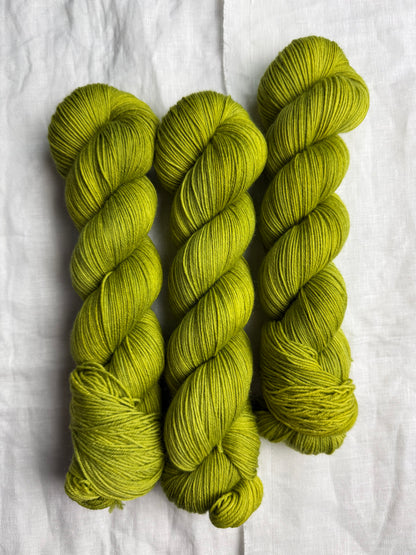 Three skeins of green yarn on a white fabric background