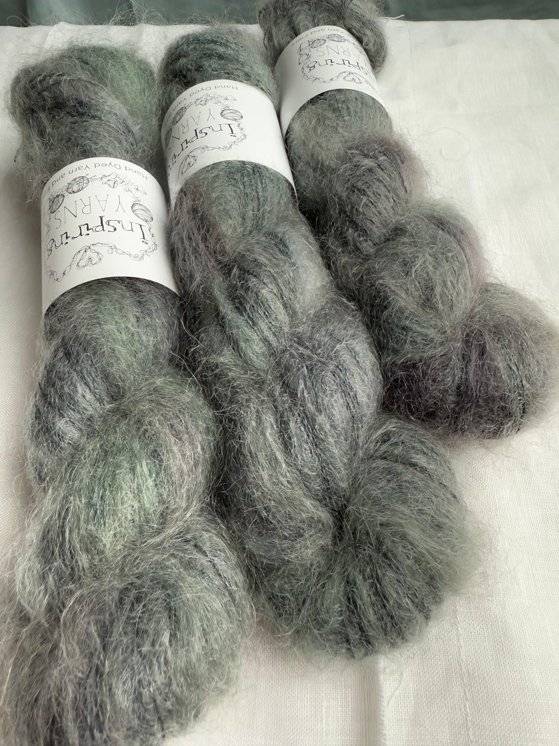 Three skeins of grey yarn with labels on a white background.